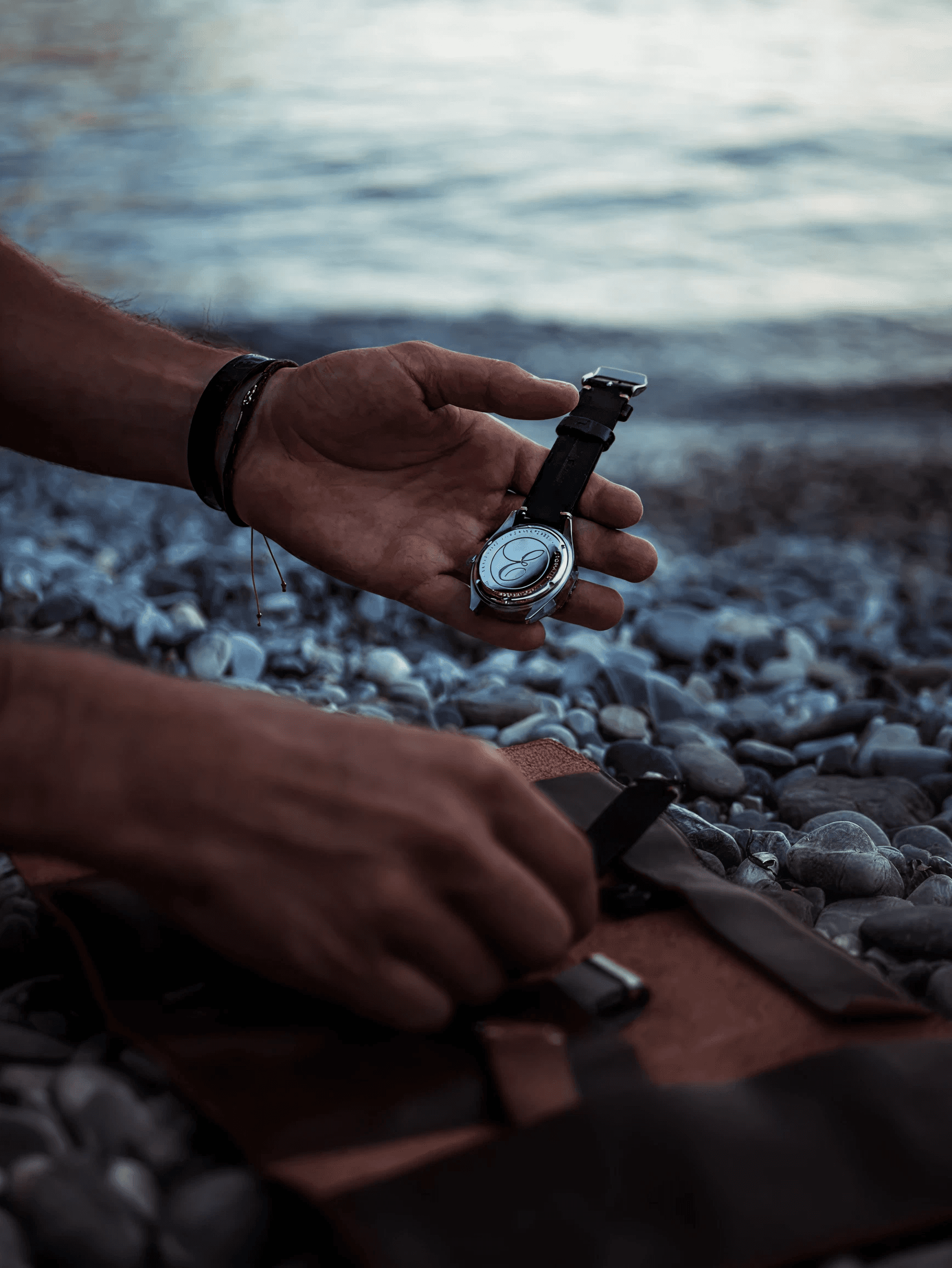 A hand holding an Eza watch beside the water